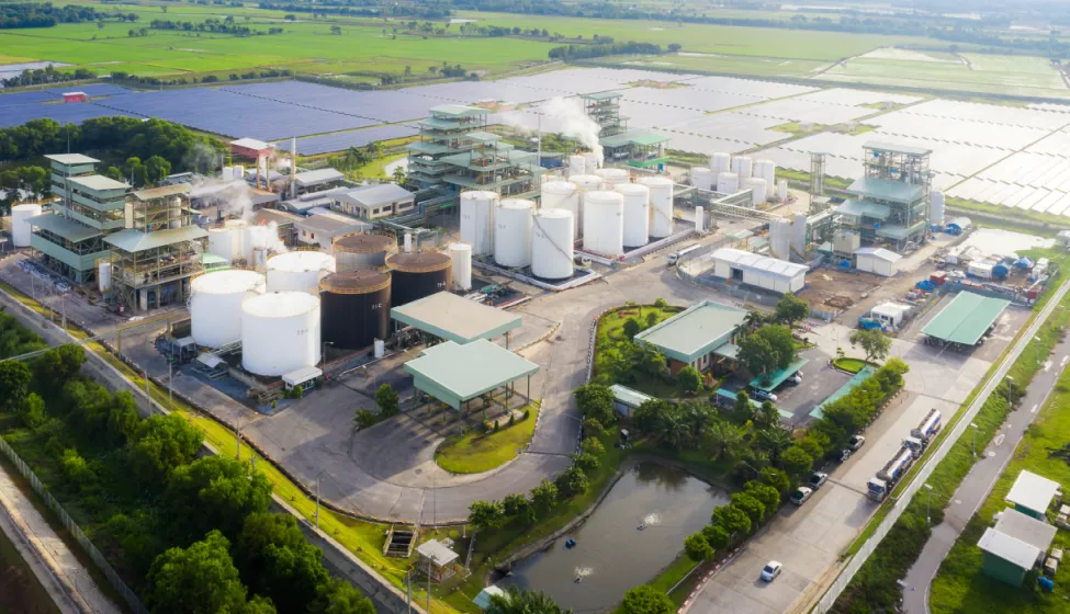 An aerial view of an industrial area with an oil refinery with multiple large storage tanks with a field filled with solar panels in the distance