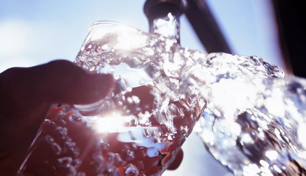 Close-up of hand holding glass under water faucet while water runs out of glass