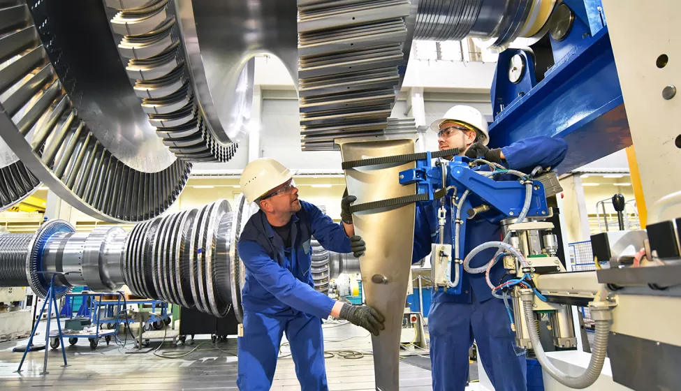 Two workers evaluate equipment on factory floor. Exponent conducts risk and safety analysis of mechanical engines. 