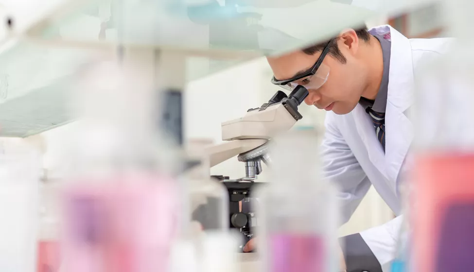 A scientist operating a microscope and examining a specimen in a slide