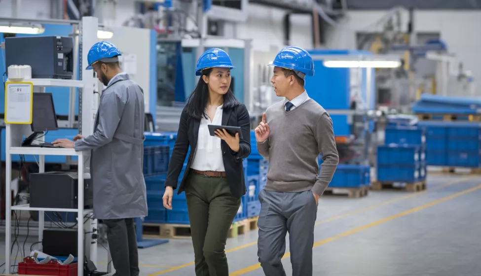 Female engineer with digital tablet talking with her colleague while walking in factory