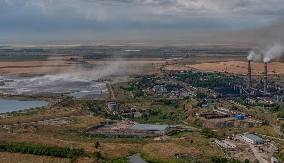 A landscape of a field containing multiple facilities and smoke stacks