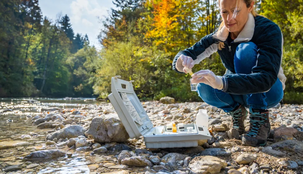 Mature female biologist adding reagent into a vial with water sample near river.