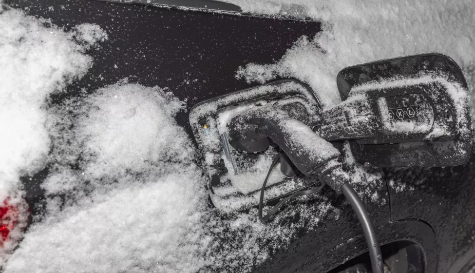 View of electric car with connected charging cable on frosty winter background