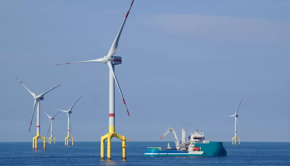 A windfarm in a body of water with a ship sailing nearby