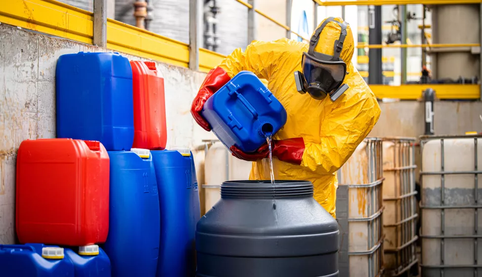 Chemical worker in yellow protection suit and gas mask making sulfuric acid for industry.