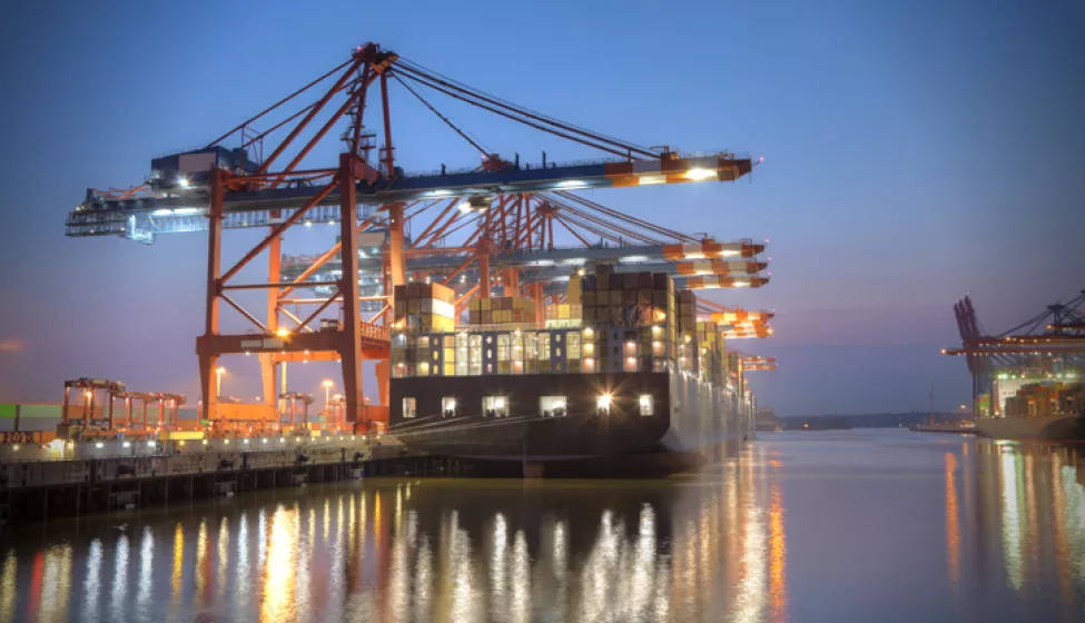 Ship docked in the harbor at night with lights reflecting off the water. Exponent provides engineering support for shipping and maritime. 