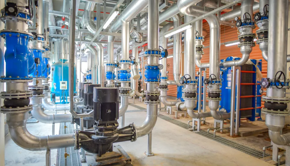 Inside view of process plant and equipment with large pipes and tubes running from floor to ceiling and across the ceiling