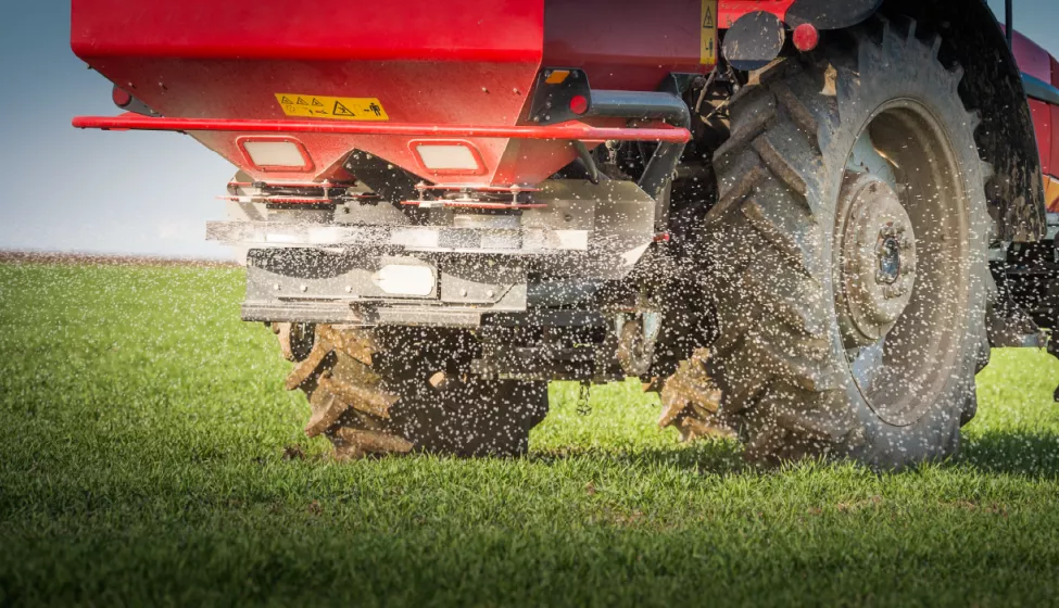 A tractor spreads fertilizer as it drives across a stretch of grass