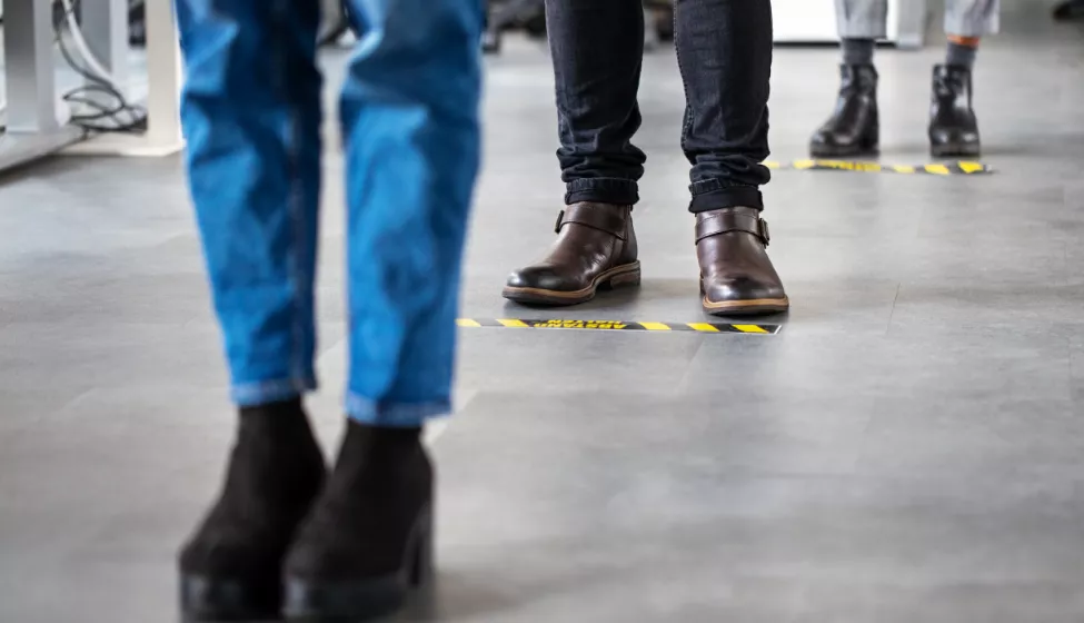 People standing on floor markers to social  distance while waiting in line 