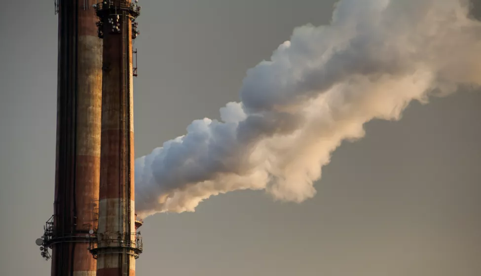 Close up view of two side-by-side smoke stacks releasing thick clouds of smoke into the air