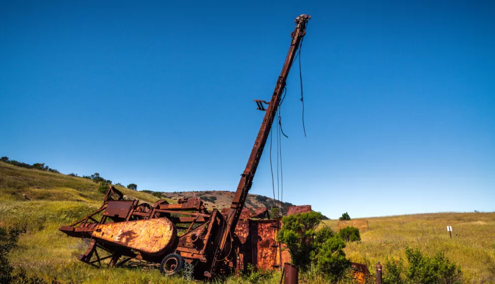 Rusty abandoned well and equipment in the middle of a hillside field