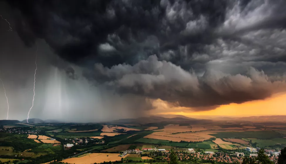 Aerial view of dark brooding storm clouds with lightening passing over urban development and open fields