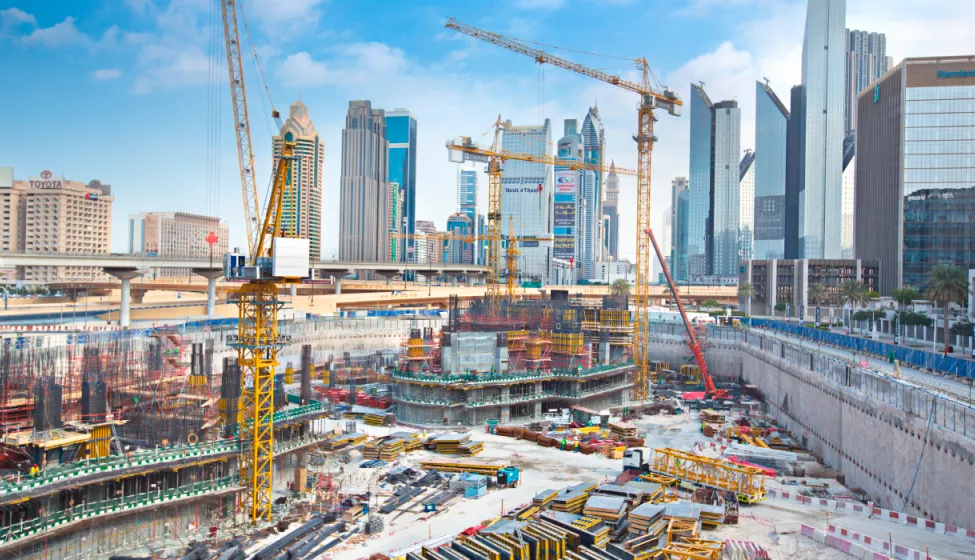 Multiple yellow cranes in large construction pit assembling a building foundation surrounded by high-rise business buildings