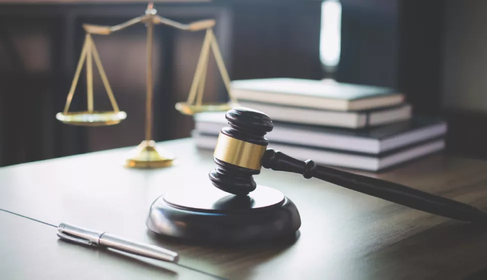 Silver pen, wooden gavel, gold scale, and stacked books on wooden desk