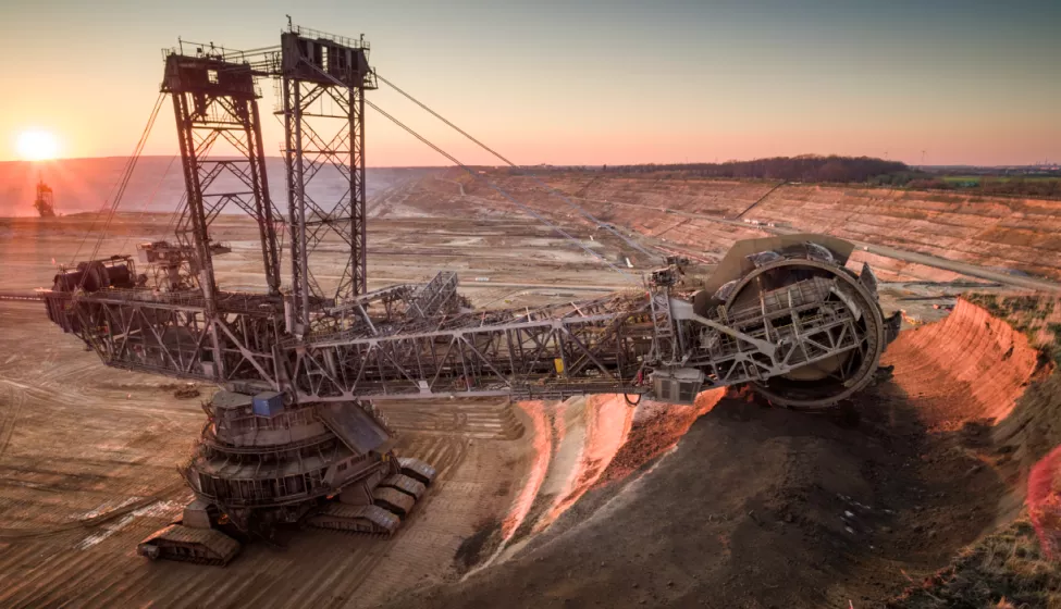 Crane-like machine excavating the earth, glowing red from sunlight, in the middle of a dirt plateau