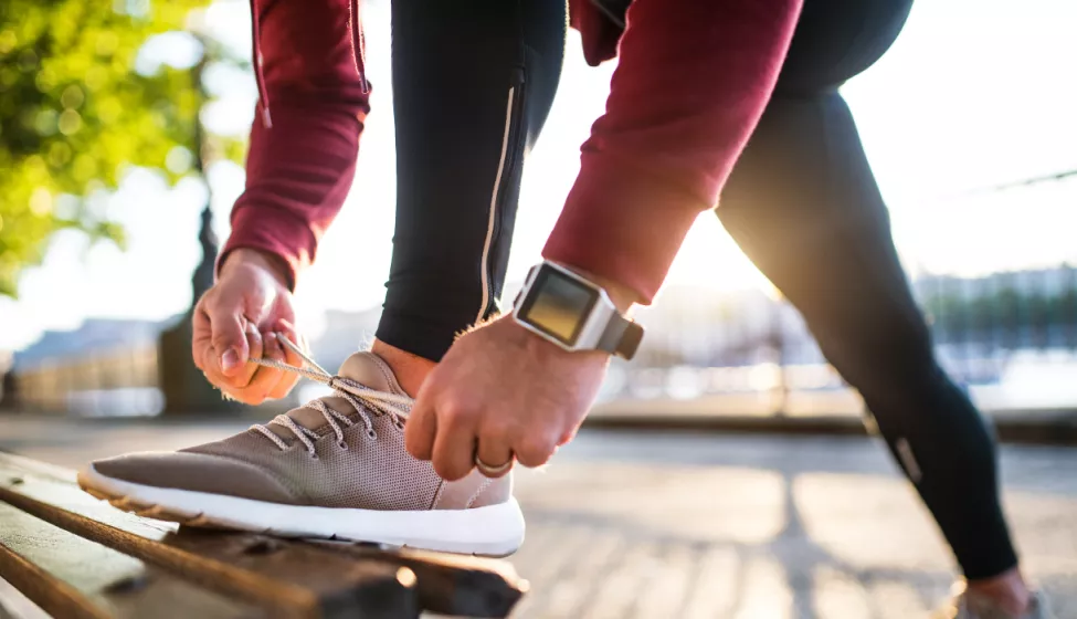 Close up of man in exercise clothing bending down to tie his shoe on a park bench