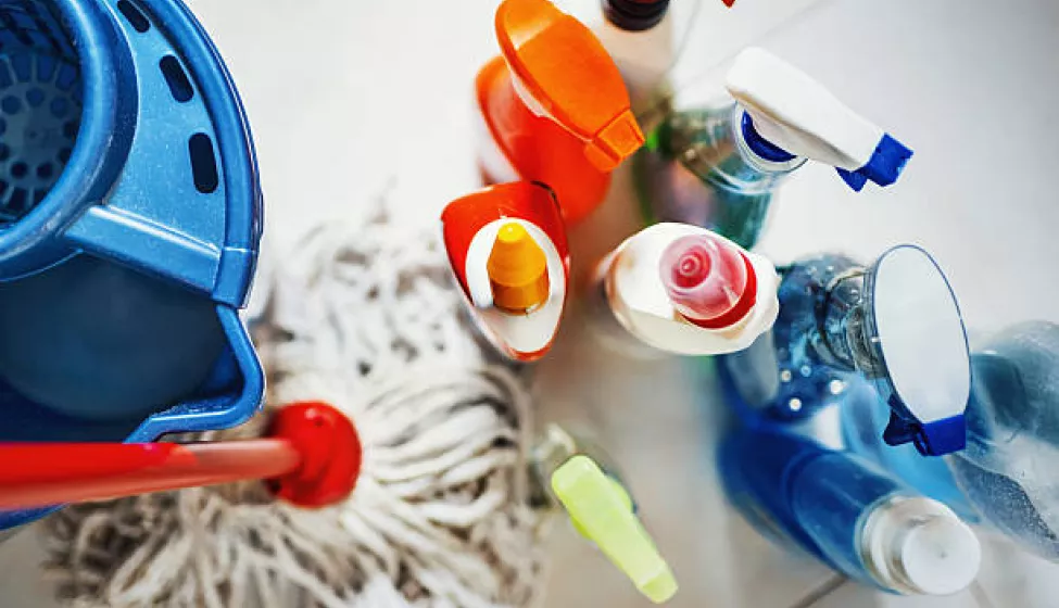 Closeup top view of unrecognizable home cleaning products with blue bucket and a mop on the side. All products placed on white tiled bathroom floor.