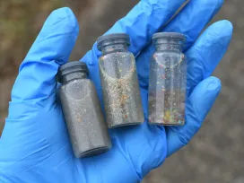 A gloved hand holding vials of water samples to test for pollution and plastic contamination