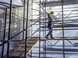 Worker balances PVC pipe while walking on scaffolding at a construction site. Exponent investigates construction accidents.