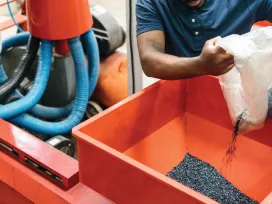 A worker pours a bag of polymer beads into a manufacturing machine. Exponent provides engineering expertise for polymers and plastics.